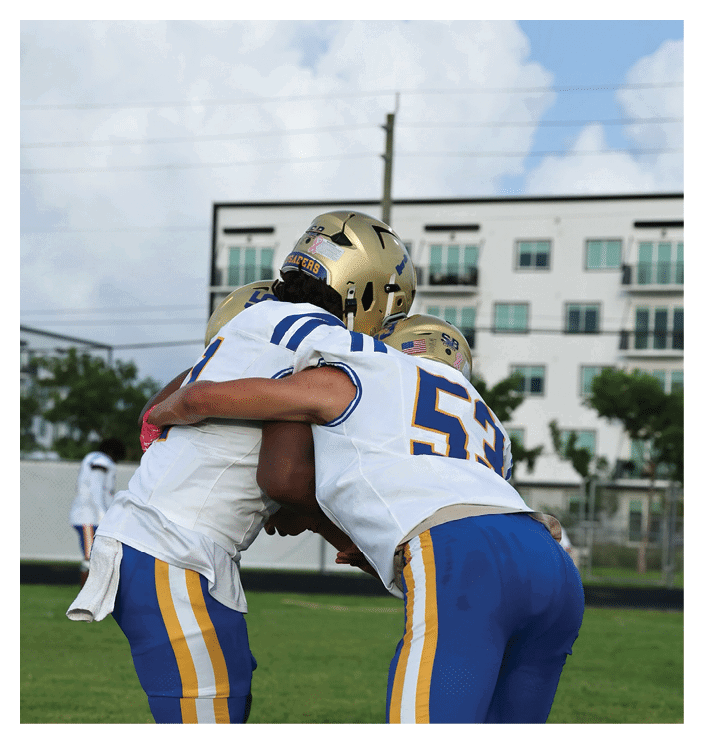 A football game is in progress with players on the field. One player is throwing a football while another player is trying to catch it. The players are wearing uniforms and are actively engaged in the game. AI generated content