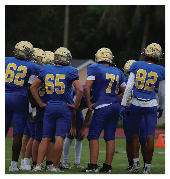 A football game is in progress with players on the field. One player is throwing a football while another player is trying to catch it. The players are wearing uniforms and are actively engaged in the game. AI generated content