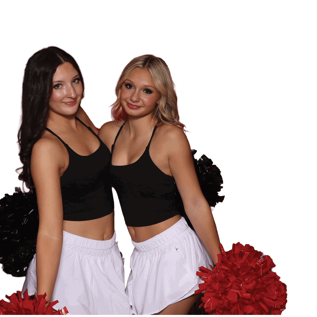 Two adults wearing black crop tops and white skirts hold red and black pom-poms while standing close together and smiling. Description generated by AI