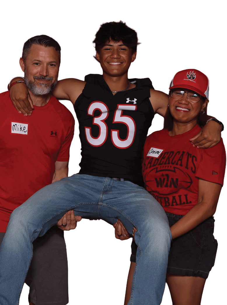 Three people are smiling with one person wearing a sports jersey being lifted by the other two who are dressed casually in red shirts. Description generated by AI