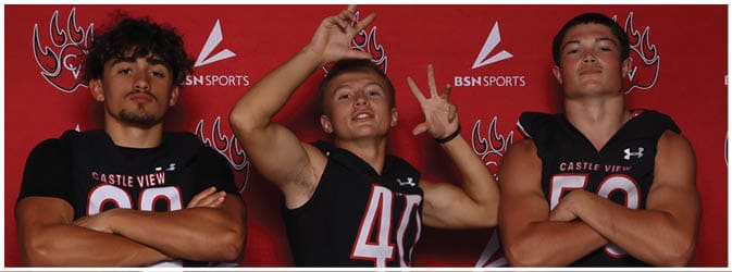 Three people wearing black sports jerseys with numbers and crossed arms stand against a red background with a sports logo. Description generated by AI