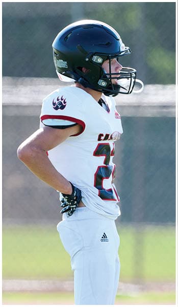 A person wearing a white football uniform with the number 21 and a black helmet stands on a field with hands on hips. Description generated by AI