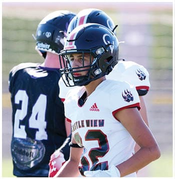 Two people wearing football helmets and uniforms stand on a field, with one in a white jersey and the other in a black jersey. Description generated by AI