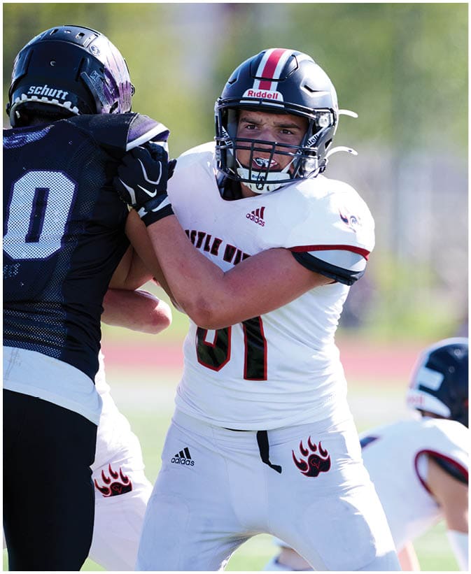 A person wearing a white football uniform and black helmet is preparing to throw a football during a game. Description generated by AI