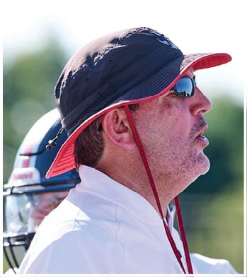 A person wearing a dark bucket hat with a red trim and sunglasses is shown in close-up from the side. Description generated by AI