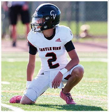 A person wearing a Castle View football uniform with the number 2 is kneeling on a grassy field while looking to the side. Description generated by AI
