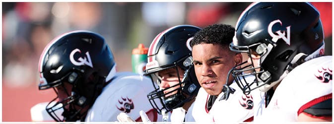 Four people wearing black helmets and white sports uniforms are sitting closely together, with one person looking intently ahead. Description generated by AI