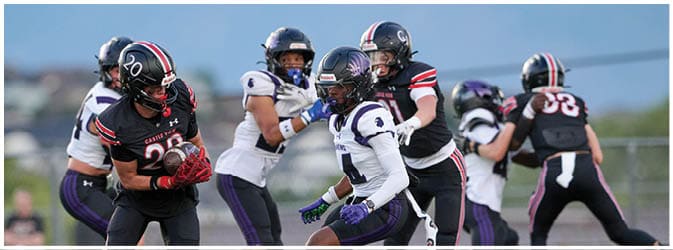 People wearing football helmets and uniforms are actively playing on a field during a game. Description generated by AI
