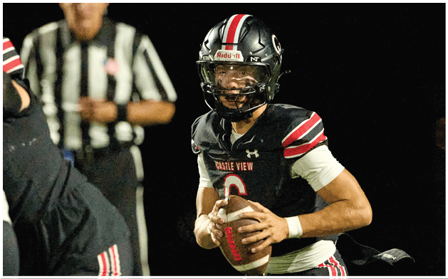 A person in a black football uniform with red and white stripes is holding a football and appears to be preparing to throw it during a nighttime game. Description generated by AI