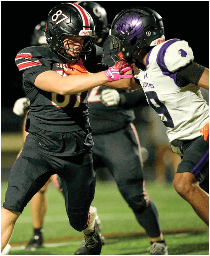 Two people wearing football helmets and uniforms are engaged in a physical play during a game, with one person pushing the other's helmet. Description generated by AI