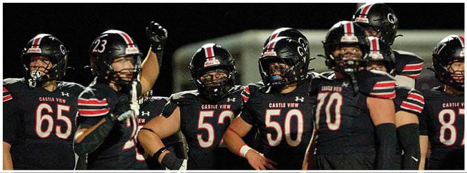 A group of people wearing black football uniforms with red and white stripes stand together on a field at night. Description generated by AI