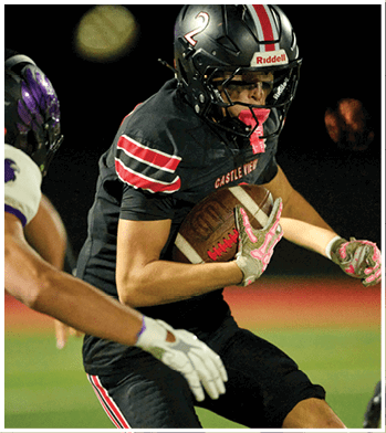 Two people in football uniforms are engaged in a play with one person holding the ball tightly while the other reaches out toward them on a field. Description generated by AI