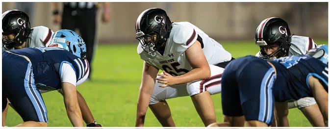 Adults in football uniforms are lined up on a field facing each other, preparing for a play during a game. Description generated by AI