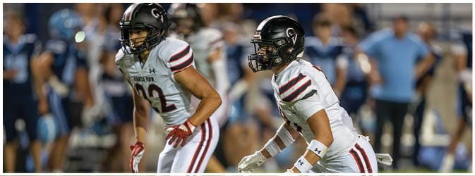 Two people in white sports uniforms with red and black stripes are actively playing on a grassy field. Description generated by AI