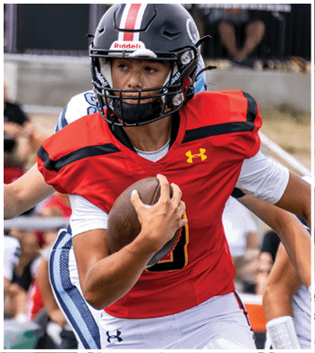 A person wearing a black helmet and red football jersey is running while holding a football tightly during a game. Description generated by AI