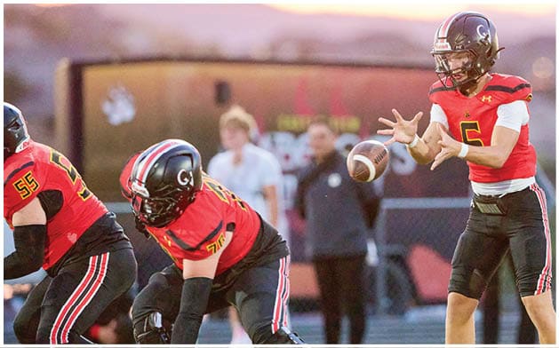 Three people in red and black football uniforms are on a field with one person preparing to throw a football. Description generated by AI