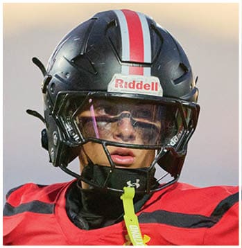 Person wearing a black football helmet with a red and white stripe and a red jersey looking ahead. Description generated by AI