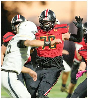 Two people in football uniforms are engaged in a play on a field, with one wearing a red and black uniform and the other in white. Description generated by AI