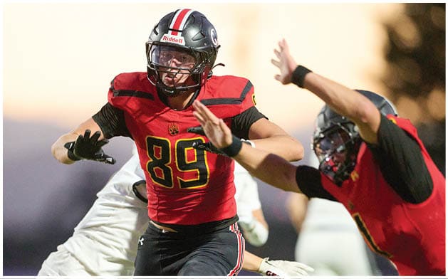 Two people in red and black football uniforms are actively engaged in a play on a field during a game. Description generated by AI