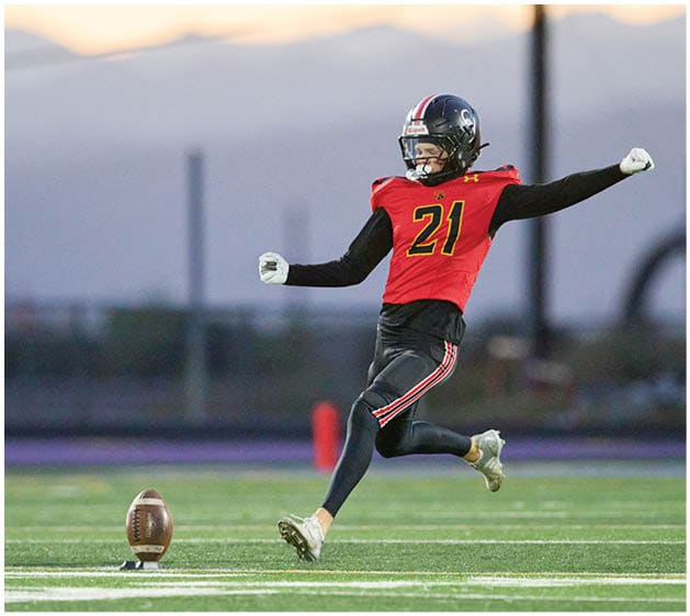 A person wearing a red sports jersey with the number 21 is kicking a football on a field during sunset. Description generated by AI