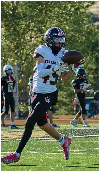 A person wearing a football uniform with the number 45 is catching a football on a field while other players in black uniforms stand in the background. Description generated by AI