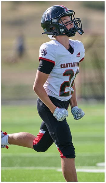 A person wearing a football uniform and helmet is running on a grassy field during a game. Description generated by AI
