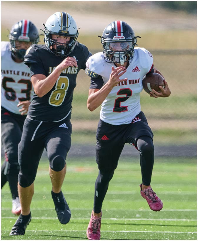 Three people wearing football helmets and uniforms are running on a field with a blurred natural background. Description generated by AI