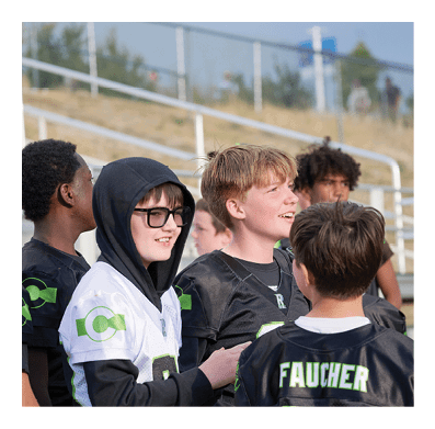 A group of children wearing football jerseys are standing together outdoors, some smiling and engaged in conversation. Description generated by AI