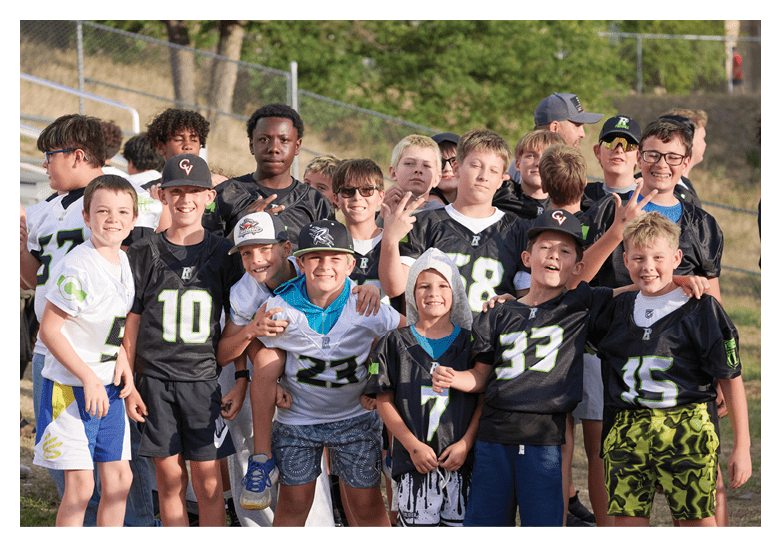 A group of children wearing sports jerseys and caps are gathered outdoors, smiling and making peace signs. Description generated by AI
