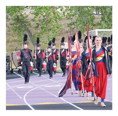 People dressed in colorful uniforms are walking on a track, some carrying flags. Description generated by AI