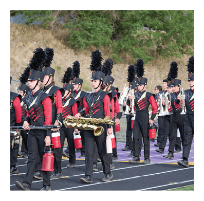 People in a marching band wearing black uniforms with red sleeves and tall black feathered hats are walking on a track while holding musical instruments and water bottles. Description generated by AI