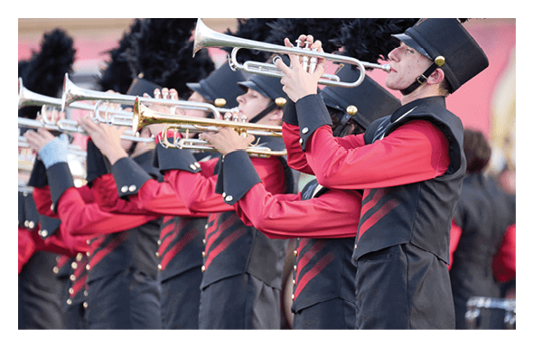 A line of people dressed in matching red and black marching band uniforms are playing trumpets in an outdoor setting. Description generated by AI