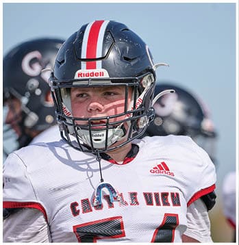 A person wearing a black football helmet and a white jersey with red lettering that reads “Castle View" is looking to the side outdoors. Description generated by AI