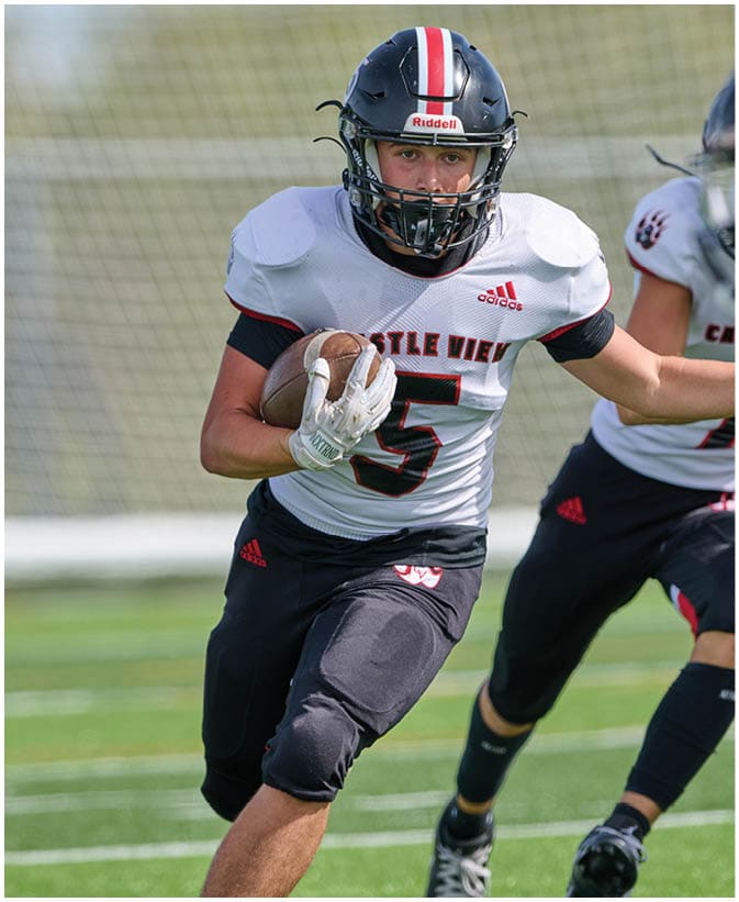 Two people wearing football uniforms are running on a field, with one person holding a football tightly. Description generated by AI