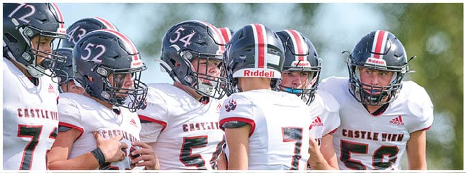 A group of people wearing football helmets and white jerseys with red and black accents are gathered closely together on a field. Description generated by AI