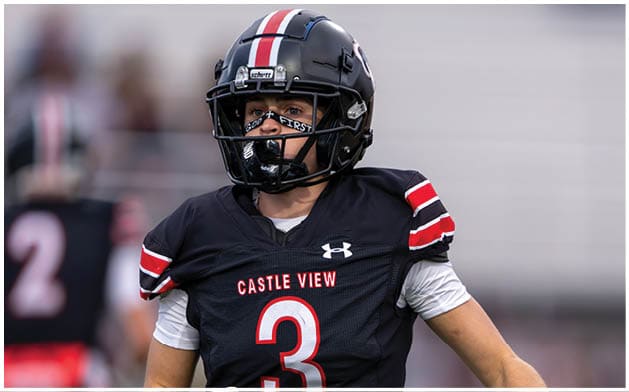 A person wearing a black football uniform with the number three and the words Castle View is on a field with another player blurred in the background. Description generated by AI