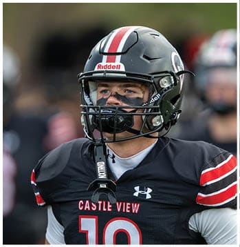 A person wearing a black football uniform with red and white stripes and the number 18 stands on a field with a helmet and black face paint. Description generated by AI