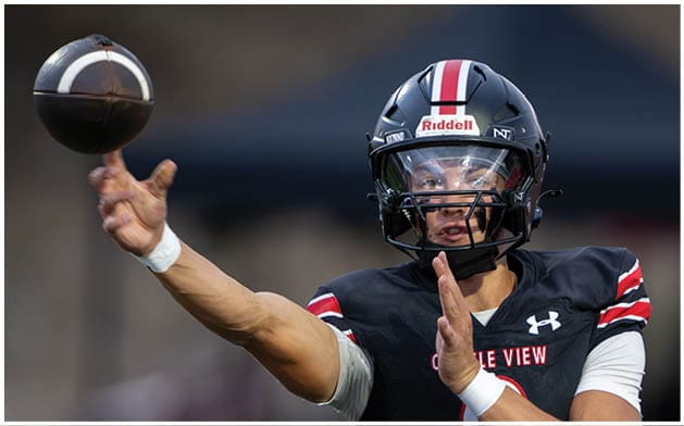 A person wearing a black football uniform and helmet is throwing a football during a game. Description generated by AI