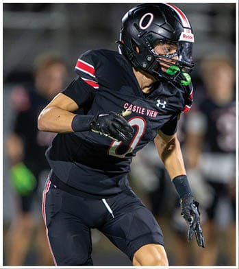 A person wearing a black sports uniform with gloves is in motion, likely participating in a football game. Description generated by AI