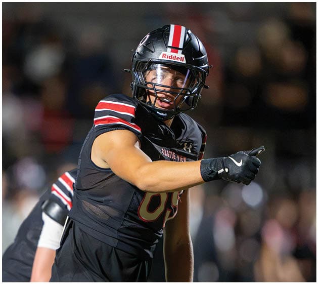 A person wearing a black football uniform and helmet is pointing forward with a focused expression during a game. Description generated by AI
