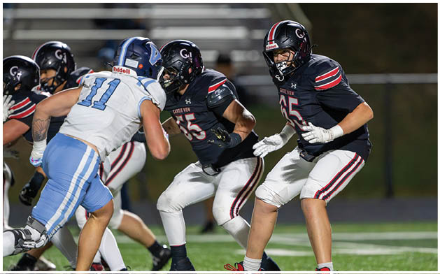 People wearing football uniforms are engaged in a play on a well-lit field during a game. Description generated by AI