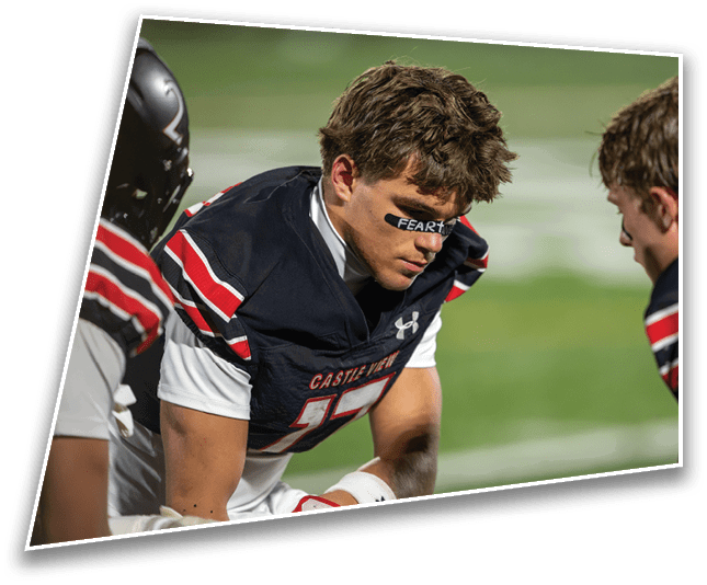 Two people in football uniforms are sitting on a bench, with one person wearing eye black that says “FEAR" and looking down thoughtfully. Description generated by AI