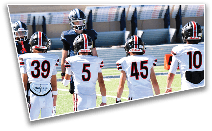 Five people in football uniforms stand on a field facing four other people in dark uniforms, with the scene captured at an angle. Description generated by AI