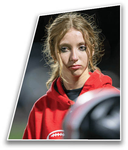 A person with curly hair wearing a red hoodie looks thoughtfully into the distance with a blurred object in the foreground. Description generated by AI