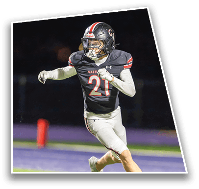 A person wearing a black football uniform with the number 21 is running on a field during a nighttime game. Description generated by AI