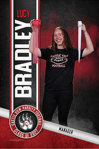 A person with curly hair wearing a black Castle View Football t-shirt is smiling and holding up two rolls of athletic tape, one red and one white, standing in front of a backdrop with the name Lucy Bradley and Castle View Varsity Football Class of 2021. Description generated by AI