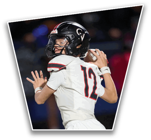 A person wearing a white football uniform with the number 12 and a black helmet is preparing to throw a football during a game. Description generated by AI
