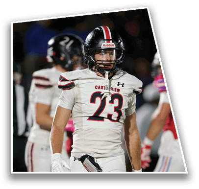 A person wearing a white football uniform with the number 23 and a black helmet stands on a field with other players in the background. Description generated by AI