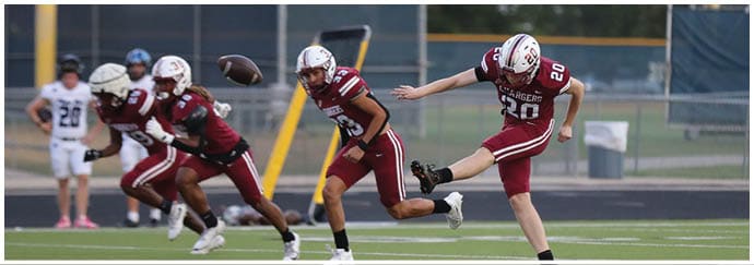 People in football uniforms are on a field with one person kicking a football while others prepare to run. Description generated by AI