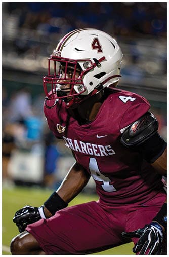A person wearing a maroon sports jersey and a white football helmet with a red faceguard is focused and appears to be preparing for a play. Description generated by AI